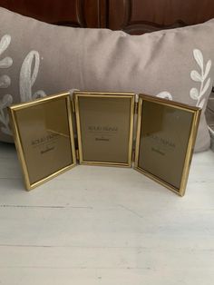 three gold framed pictures sitting on top of a white table next to a pillow and pillows