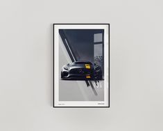 a black sports car parked in front of a window on a white wall next to a framed photograph