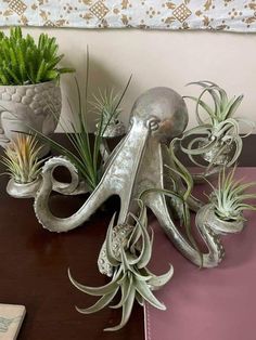 an octopus sculpture sitting on top of a table next to potted plants and succulents