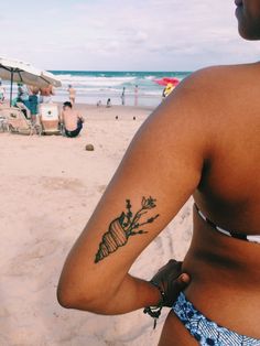 a woman with a tattoo on her left arm standing in front of the ocean and beach