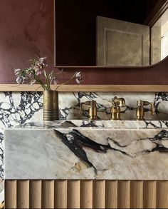 a marble sink with gold faucets and flowers in the vase next to it