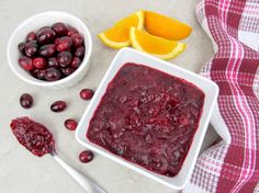 cranberry sauce in a white bowl next to orange slices and spoons on a table