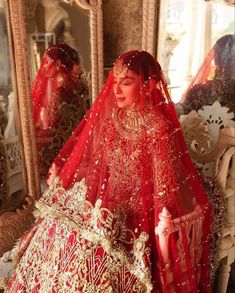 a woman in a red and gold bridal gown looking at herself in the mirror