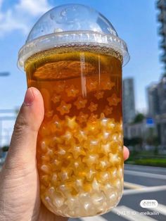 a person holding up a plastic cup filled with liquid in the middle of a street