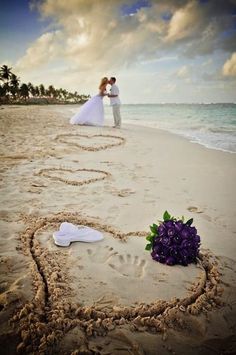 a bride and groom standing in the sand at the beach with their names written in the sand