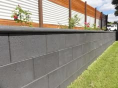 a concrete retaining wall with flowers growing on it's top and grass in the foreground