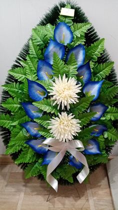 a blue and white christmas tree with flowers on it's top, surrounded by greenery