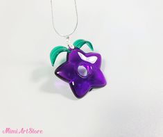 a purple and green flower shaped glass pendant on a silver plated chain necklace is shown against a white background