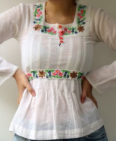 "Beautiful vintage 70's Indian white blouse floral embroidered detailing in pink, yellow, blue, green and brown, cotton, long sleeves, five buttons down the bodice, high waist with a belt tied at the back for an adjustable fit, original tag intact, aside from minor signs of wear, including ultra-faint amber marking under the arms, otherwise good vintage condition clean, ready to wear.**Model is 5'8\" and a size S/M for reference ** tag size: M Approximate size: S - Please refer to the measuremen White Cotton Hippie Blouse, Hippie Long Sleeve Tops With Floral Embroidery, Vintage Long Sleeve Top With Multicolor Embroidery, Cotton Long Sleeve Blouse With Yoke Detail, Long Sleeve Cotton Blouse With Yoke Detail, Long Sleeve Cotton Blouse With Yoke, Bohemian Long Sleeve Tops With Yoke Detail, Spring Cotton Top With Yoke Detail, Fitted Folk Style Long Sleeve Tops