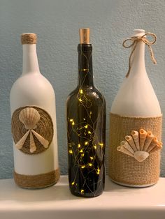 three wine bottles decorated with seashells and twine string lights are sitting on a shelf