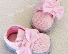 two crocheted baby shoes with pink bows on the front and blue bottom, sitting on a white blanket