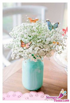 a vase filled with white flowers and butterflies on top of a wooden table next to a doily