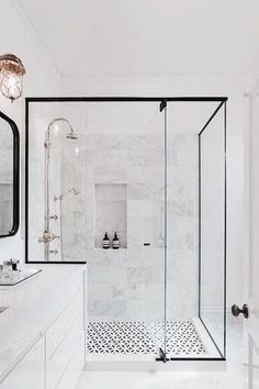 a white bathroom with black accents and marble counter tops, shower stall, and double sinks