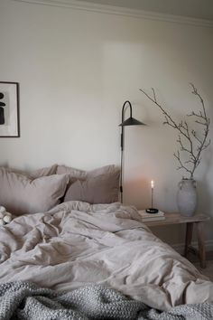 an unmade bed with white sheets and pillows in a bedroom next to a lamp