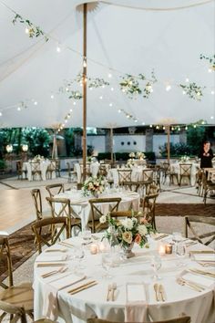 tables and chairs are set up in a tent for an outdoor wedding reception with lights strung from the ceiling