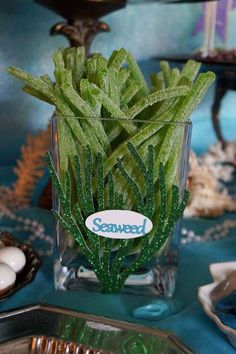 a glass vase filled with green plants sitting on top of a blue tablecloth covered table