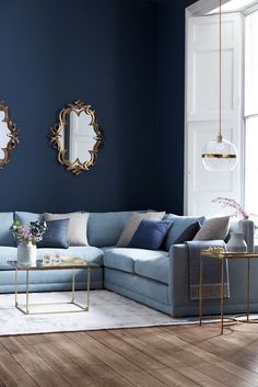 a living room with blue walls and gold mirrors on the wall, along with two couches