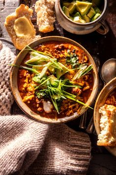 two bowls filled with food on top of a wooden table next to bread and spoons