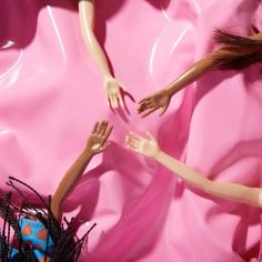 two dolls reaching for each other on a pink surface