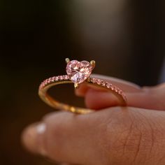 a close up of a person's hand holding a ring with a pink diamond