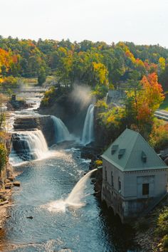 a river running through a lush green forest next to a small building with a waterfall coming out of it