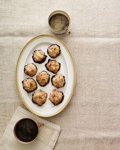 a white plate topped with small cookies next to a cup of coffee and saucer