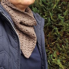 a woman standing in front of a bush wearing a knitted cowl and scarf