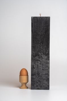 an egg is sitting next to a tall black block with a wooden stand on it