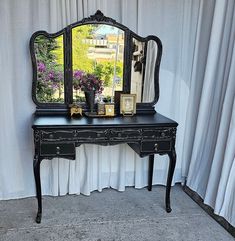 a black desk with a mirror and vase on it next to a curtained window