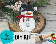 a snowman ornament sitting on top of a piece of wood next to paintbrushes