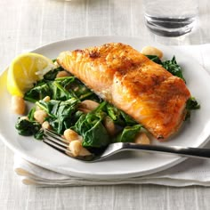 a white plate topped with fish and spinach next to lemon wedges on a table