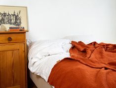 a bed with an orange blanket on top of it next to a night stand and nightstand