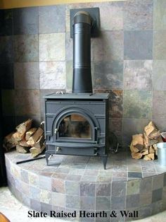 a wood burning stove sitting on top of a stone wall next to a pile of firewood