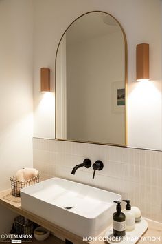 a white sink sitting under a large mirror next to a wooden shelf with soap bottles on it