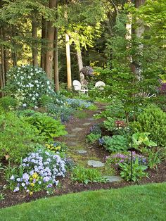 a garden with lots of flowers and trees in the background, along with a stone path