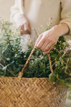 a woman is holding a basket with plants in it and tying the handle to one of the baskets