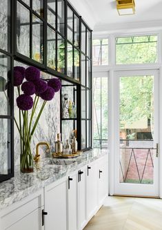 a kitchen with white cabinets and marble counter tops, gold faucets and purple flowers