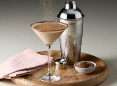 a drink in a glass next to a shaker on a wooden tray with a pink napkin