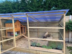 a wooden structure with a blue roof and some plants in the back ground next to it