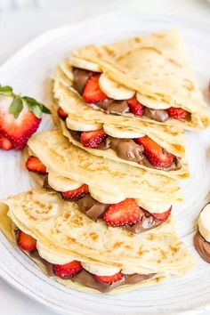 pancakes with chocolate and strawberries are on a white plate next to some sliced bananas