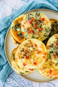 four mini muffins with cheese and toppings on a white plate next to a blue napkin