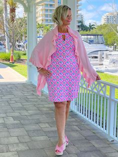 a woman in a pink and blue dress is standing on a porch next to a white fence