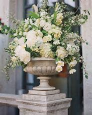 a large vase with flowers in it sitting on a pedestal outside an old stone building