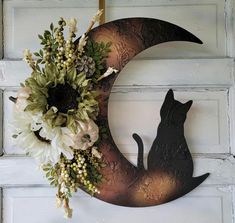 a black cat sitting on top of a metal moon with flowers in it's mouth