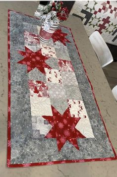 a quilted table runner with red and white stars on it, next to a potted plant