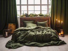 a bed with green sheets and pillows in front of a large window filled with candles