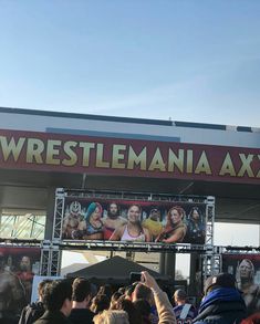 a crowd of people standing in front of a building with a wrestling poster on it