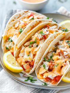 three tacos on a plate with lemon wedges