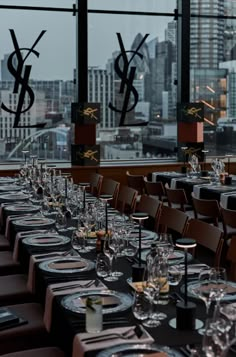 a long table set up with wine glasses and place settings in front of large windows overlooking the city