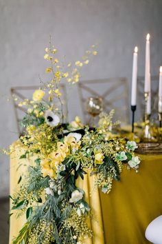 the table is set with yellow linens and white flowers, greenery and candles